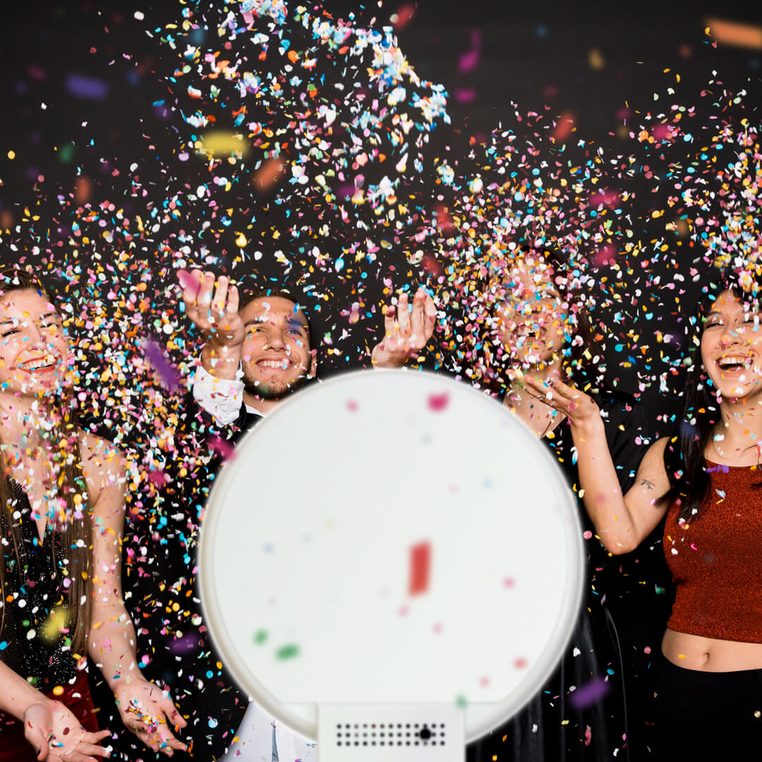 Four friends throw confetti in the air in front of a white photo booth